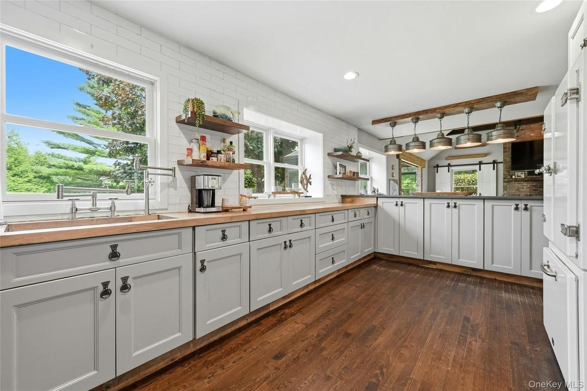 Kitchen featuring wood-finish flooring, light gray cabinetry with dark hardware, butcher block countertops, white subway tile backsplash, and multiple