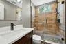 Walk-in shower featuring wood-finish wall tile, pebble floor, and glass enclosure