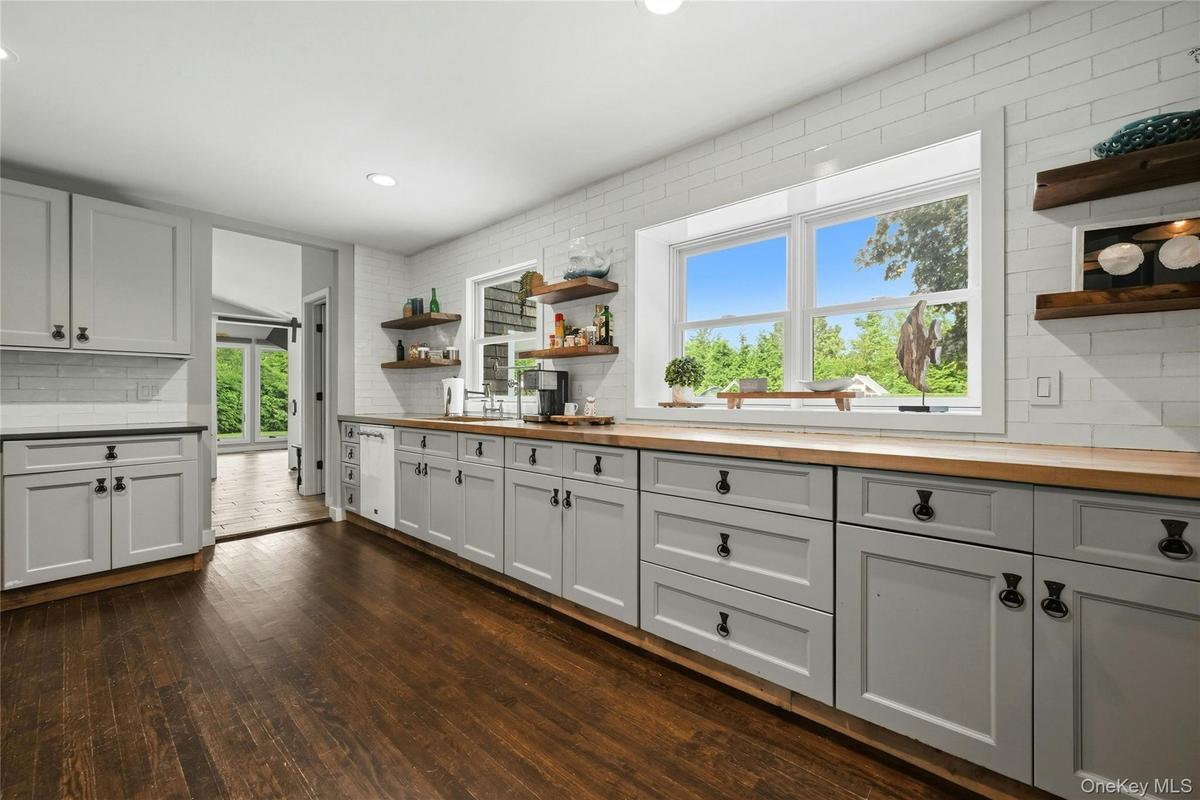 Spacious kitchen featuring gray shaker-style cabinetry with dark hardware, wood-finish countertops, and white subway tile backsplash