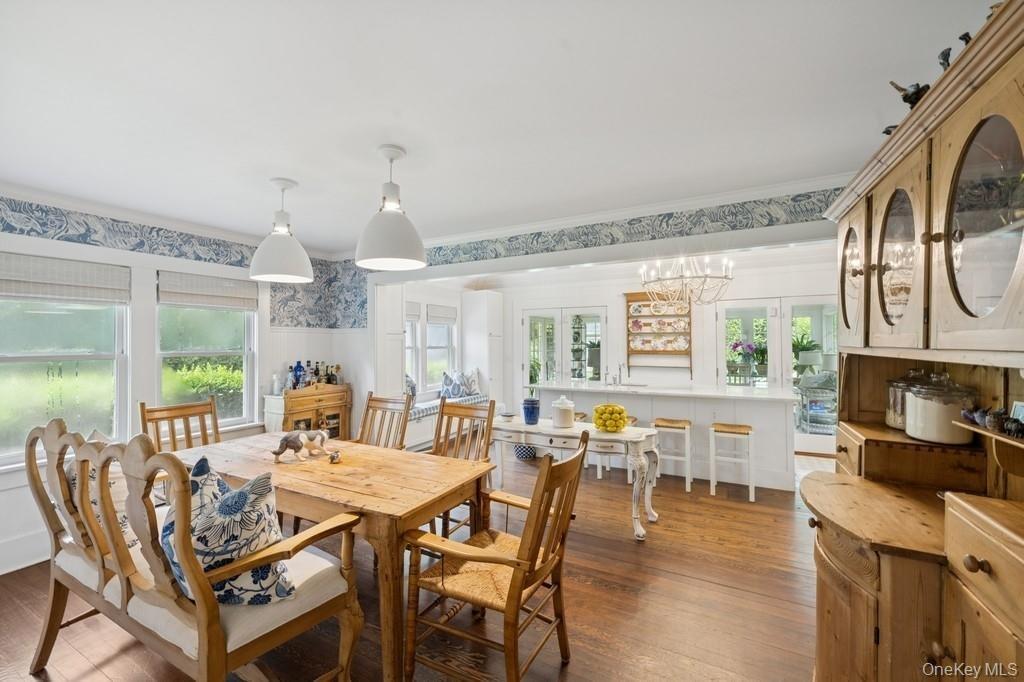 Dining room with dark wood-type flooring, a chandelier, ornamental molding, wallpapered walls, and wainscoting