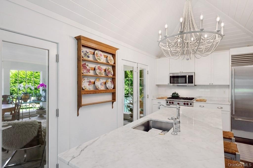 Kitchen featuring stainless steel appliances, a chandelier, healthy amount of natural light, vaulted ceiling, and tasteful backsplash