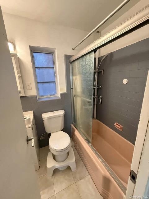 Built-in bathtub with sliding glass enclosure, white ceramic commode, and tiled flooring