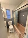 Built-in bathtub with sliding glass enclosure, white ceramic commode, and tiled flooring