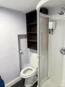 Corner shower enclosure with an integrated showerhead, and a wall-mounted shelving unit