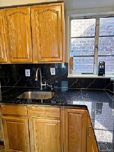 Natural wood-finish cabinetry, black stone countertops, undermount stainless steel sink, pull-down faucet, and a black stone backsplash