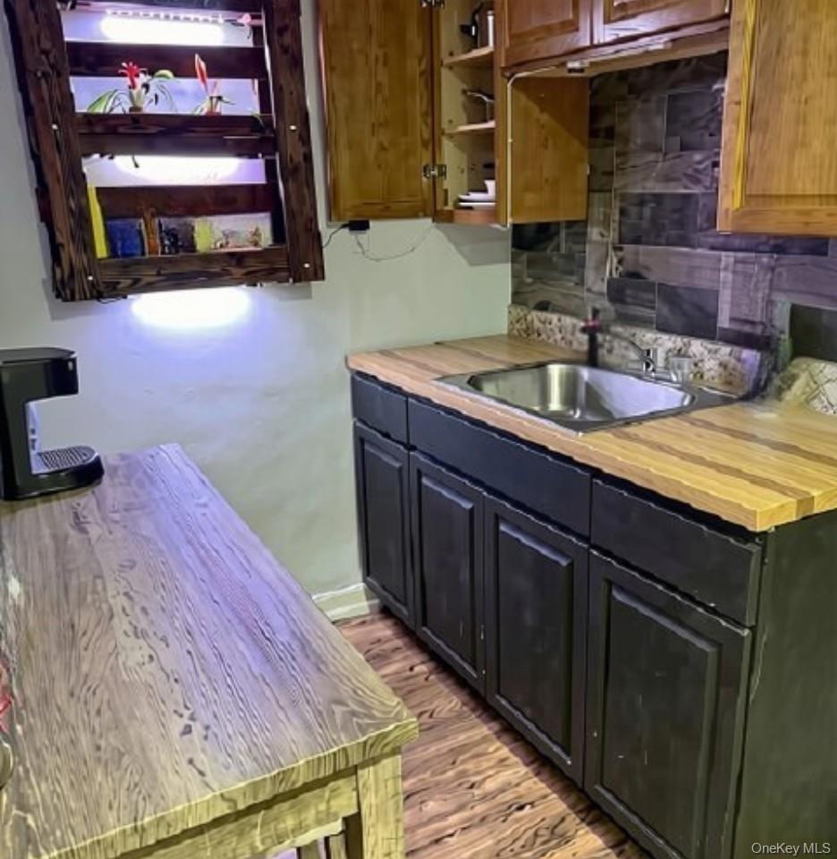 Wood-finish flooring, dark wood-finish base cabinetry, stainless steel sink, wood-finish countertops, and upper wood-finish cabinetry