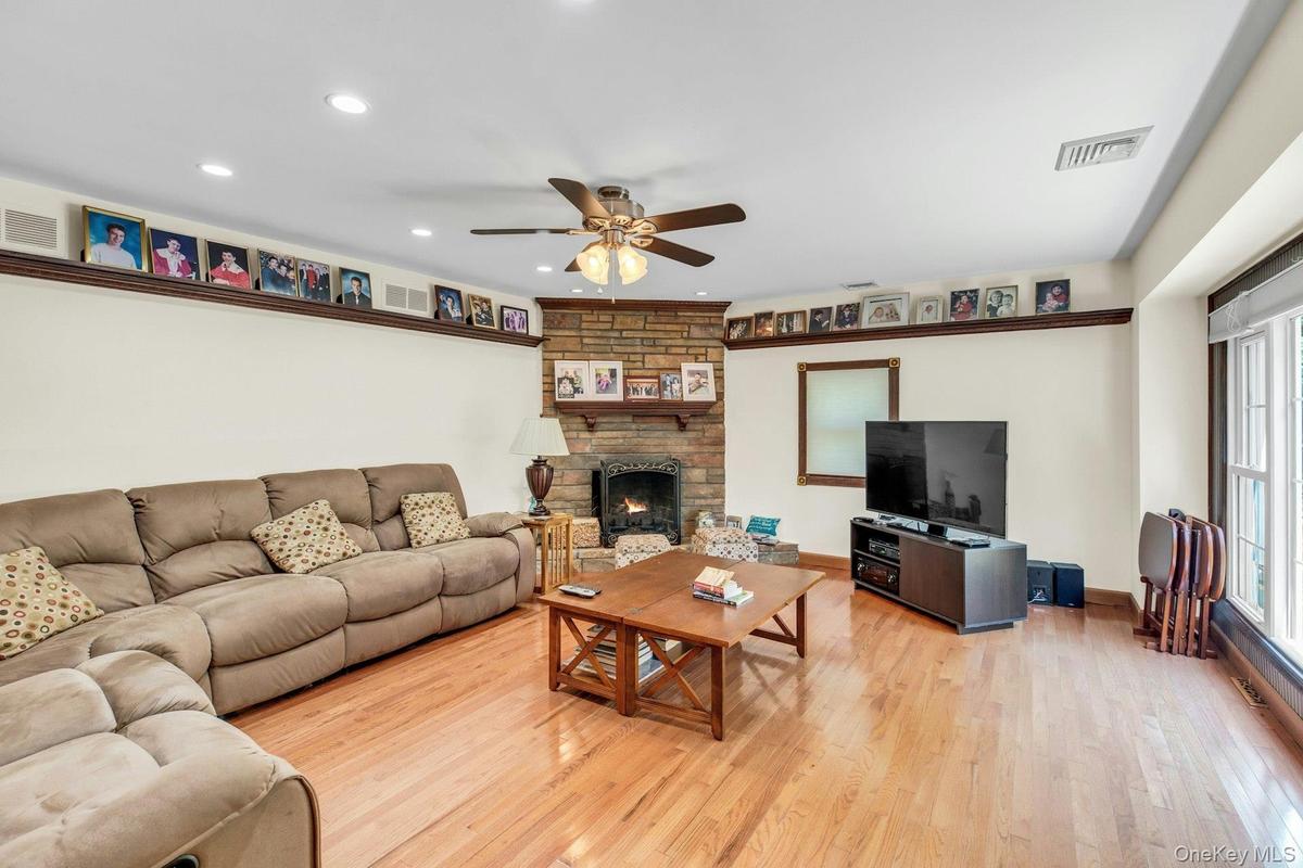 Living room featuring hardwood flooring, a stone-clad fireplace with mantel, recessed lighting, and a ceiling fan