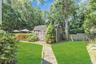 Expansive backyard oasis featuring a meticulously manicured lawn, mature tree-lined perimeter, and charming detached storage shed with X-brace detaili