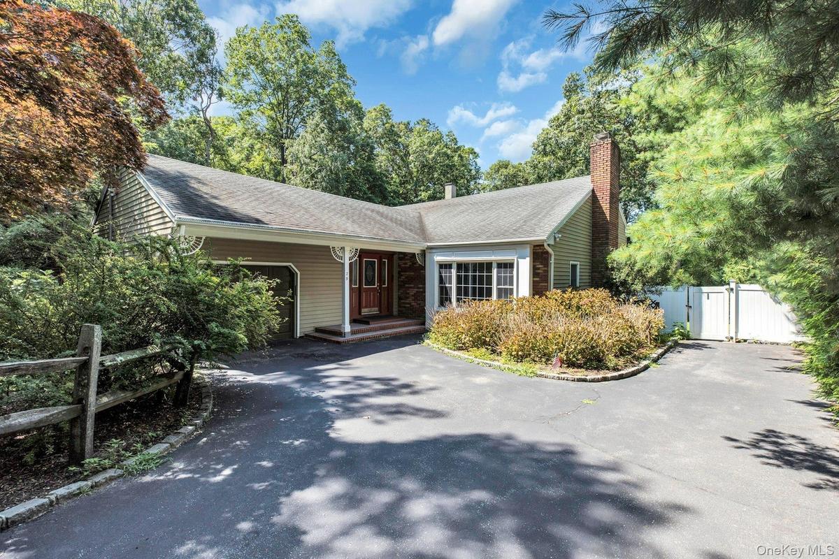 Charming ranch-style home featuring a welcoming brick chimney, composite siding exterior, and asphalt driveway