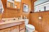 Warm wood-paneled bathroom featuring a wood-finish vanity with integrated sink, ceramic countertop, and ample storage cabinetry