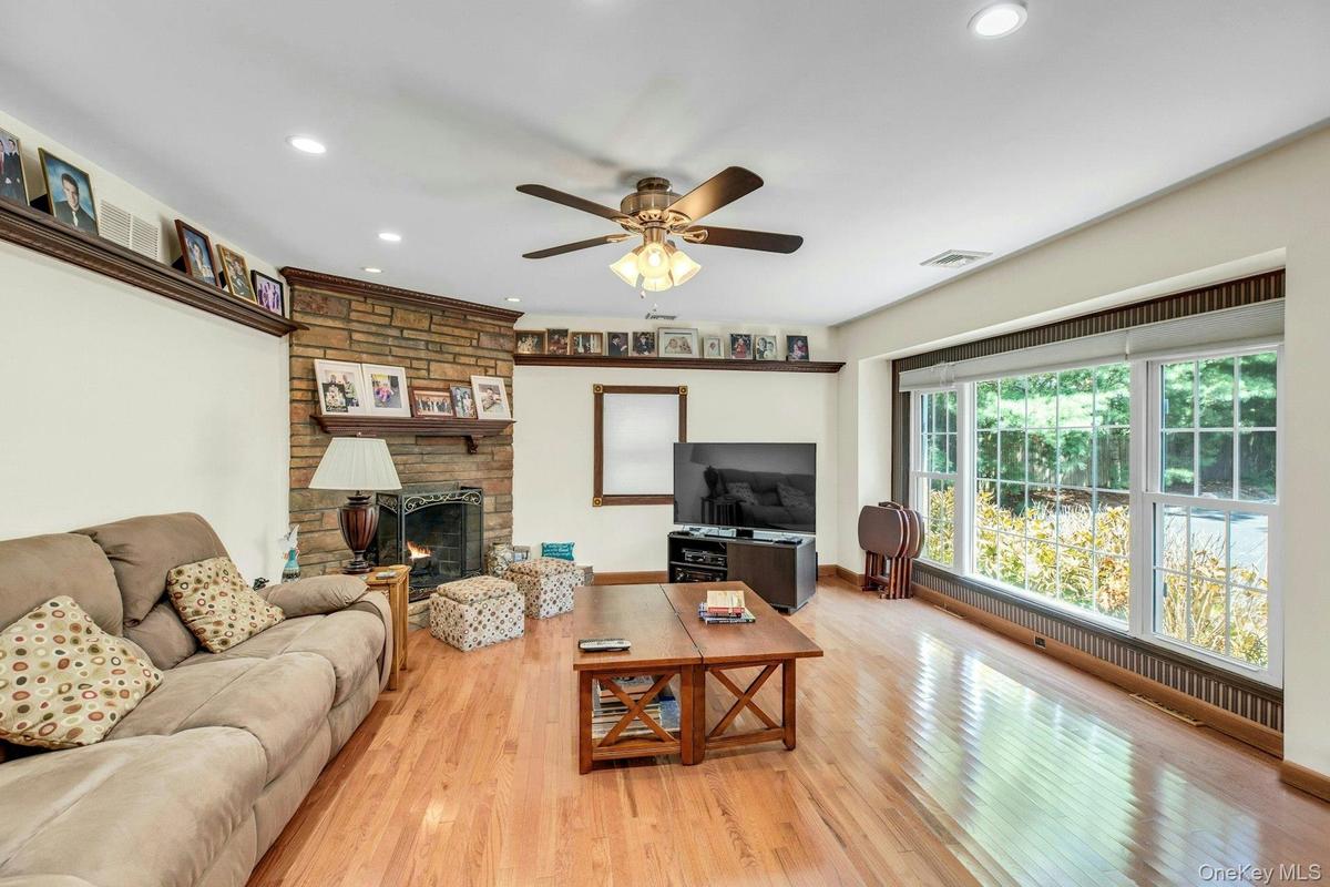 Living area featuring hardwood flooring, a stone-front fireplace with mantel, recessed lighting, and a ceiling fan