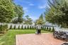 Expansive backyard featuring a brick paver patio, a manicured lawn, a white lattice fence, mature trees, and evergreen landscaping