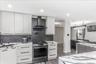 Modern kitchen featuring light wood-finish cabinetry, dark horizontal hardware, and a stainless steel gas range with a coordinating range hood