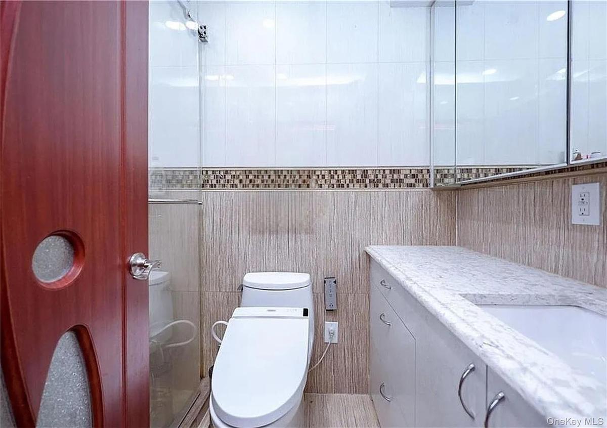 Bathroom featuring a modern toilet, glass-enclosed shower, built-in vanity with integrated sink, and a mirrored medicine cabinet