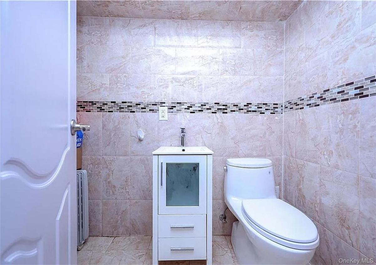 Modern bathroom featuring ceramic tile walls with decorative mosaic border stripe, a white vanity with integrated sink and storage drawers, contempora