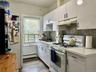 Kitchen featuring white appliances, white cabinetry, light countertops, under cabinet range hood, and dark wood finished floors