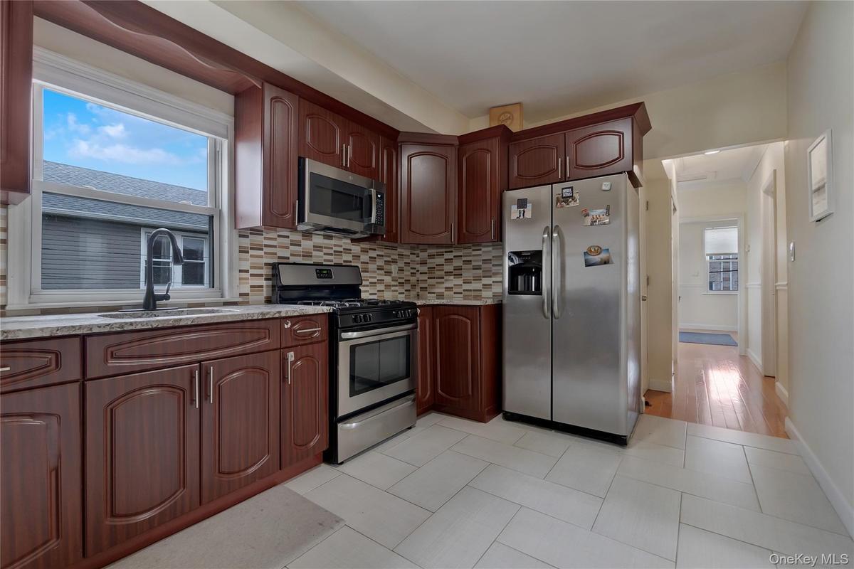 Kitchen featuring wood-finish cabinetry, stainless steel appliances, a multi-tone tile backsplash, and light-toned tile flooring