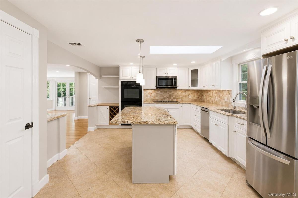 Spacious kitchen featuring an island with granite countertops, tile flooring, white cabinetry, stainless steel appliances, and a skylight