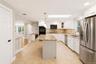 Spacious kitchen featuring an island with granite countertops, tile flooring, white cabinetry, stainless steel appliances, and a skylight