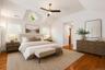Spacious bedroom featuring vaulted ceilings, wood-finish flooring, and multiple windows including a prominent diamond-shaped window