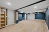 Spacious basement room featuring light wood-finish flooring, recessed lighting, accent walls, built-in shelving, and white trim