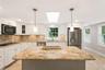 Kitchen featuring a central island with a stone countertop, white cabinetry, integrated stainless steel appliances, a tile backsplash, and recessed li