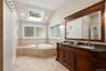 Bathroom featuring a built-in corner jet tub with tiled surround, a large skylight, vaulted ceiling, and recessed lighting