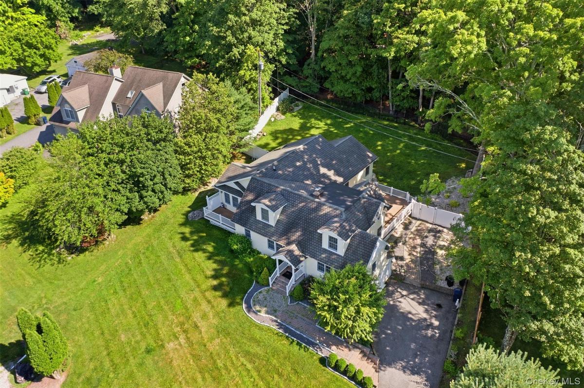Expansive aerial perspective showcasing a residential property with a multi-level deck, a paved driveway, and mature landscaping