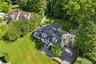 Expansive aerial perspective showcasing a residential property with a multi-level deck, a paved driveway, and mature landscaping