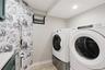 Dedicated laundry area featuring a front-load washer and dryer set on pedestals, recessed lighting, patterned accent wall, and a folding drying rack