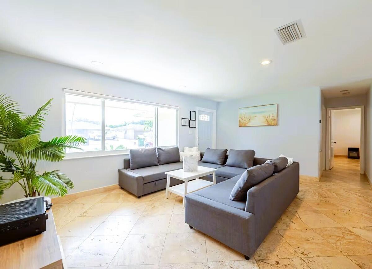 Bright living space featuring large sliding windows, light-colored tile flooring, recessed ceiling lighting, and a white entry door with frosted glass