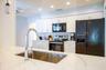 Kitchen featuring white shaker cabinetry, stainless steel sink with gooseneck faucet, light-toned countertop with veining, black appliances, and reces