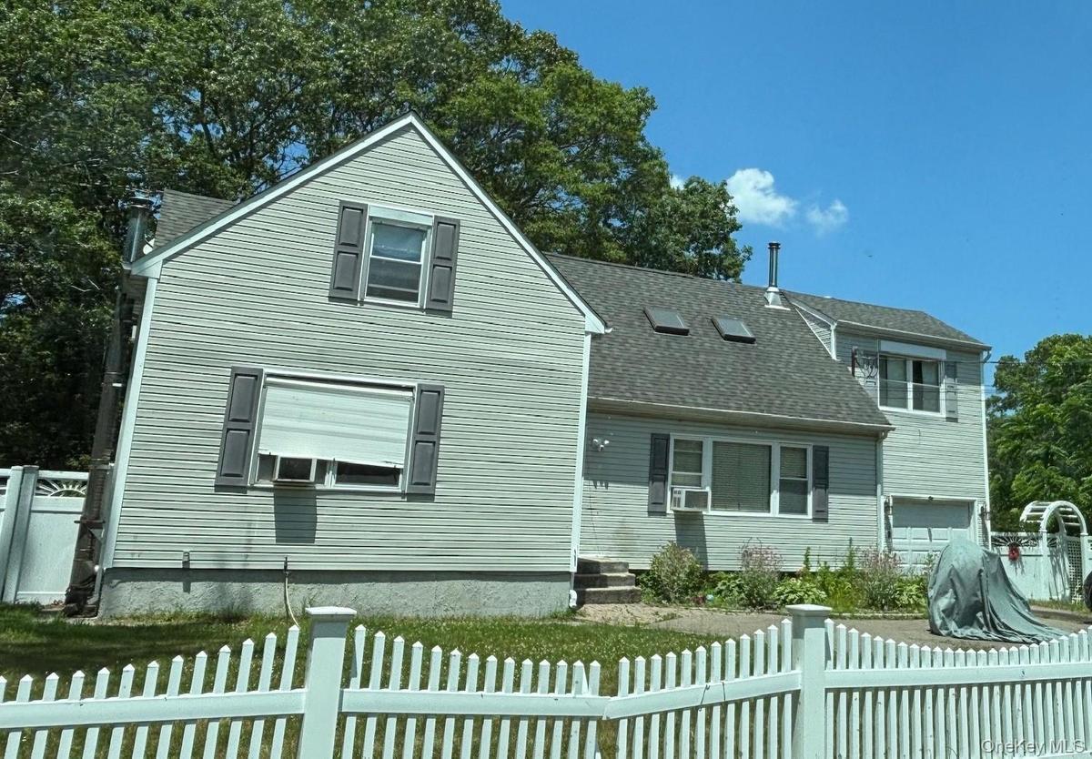 Traditional home featuring a shingled roof, a fenced front yard, and a garage