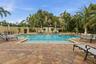 Community pool with sun shelf, spa, and ample chairs on the beautiful paver deck surrounded by lush landscaping