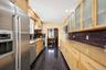 Galley kitchen featuring stainless steel appliances, light wood-finish cabinetry, granite-style countertops, and a dark tile backsplash