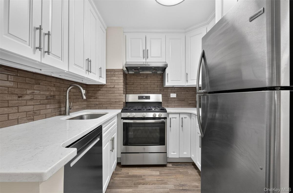 Updated kitchen with stainless steel appliances, including a gas range, exhaust range hood, full size dishwasher, stone counters, and modern hardware.