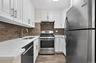 Updated kitchen with stainless steel appliances, including a gas range, exhaust range hood, full size dishwasher, stone counters, and modern hardware.