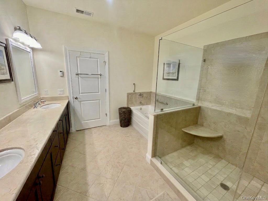 Bathroom featuring a dual vanity with undermount sinks, a built-in soaking tub, a glass-enclosed shower with a built-in corner shelf, tile flooring, a