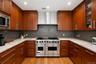 Gourmet kitchen featuring a stainless steel gas range, wood-finish cabinetry, light-toned countertops, tile backsplash, and recessed lighting
