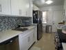 Modern kitchen featuring white shaker cabinetry, light-toned countertops, a mosaic tile backsplash, stainless steel appliances, and tile flooring