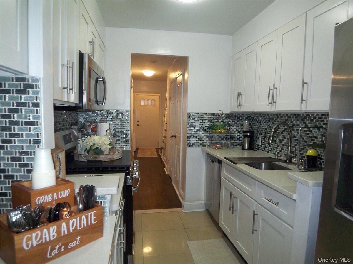 Galley kitchen featuring white shaker cabinetry, stainless steel appliances, a tiled backsplash, and light-tone countertops