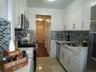 Galley kitchen featuring white shaker cabinetry, stainless steel appliances, a tiled backsplash, and light-tone countertops