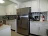 Modern kitchen featuring a stainless steel side-by-side refrigerator, white shaker-style cabinetry, light-toned countertops, a mosaic tile backsplash,