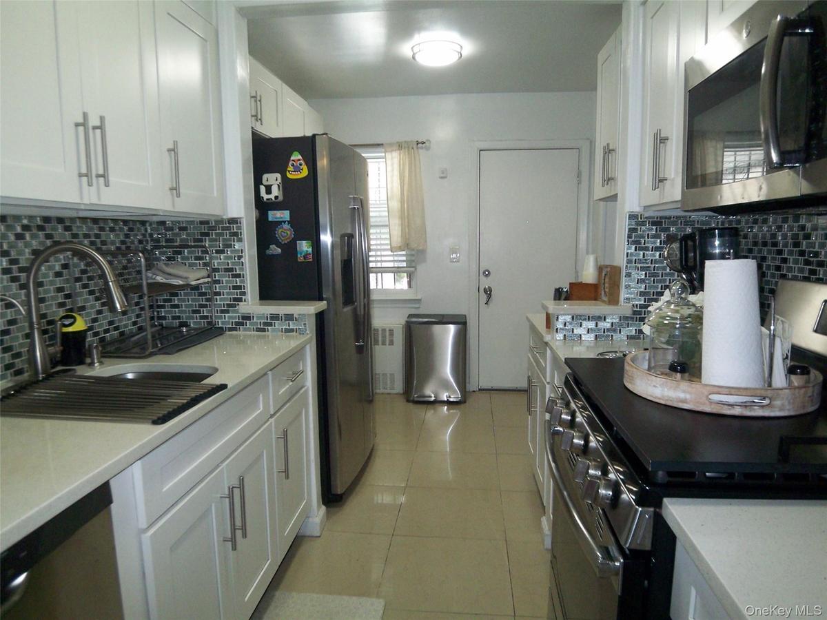 Galley kitchen featuring white cabinetry with brushed nickel pulls, light-toned countertops, and a mosaic tile backsplash