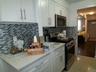 Modern kitchen featuring white cabinetry with brushed nickel hardware, light-toned countertops, and a full tile backsplash