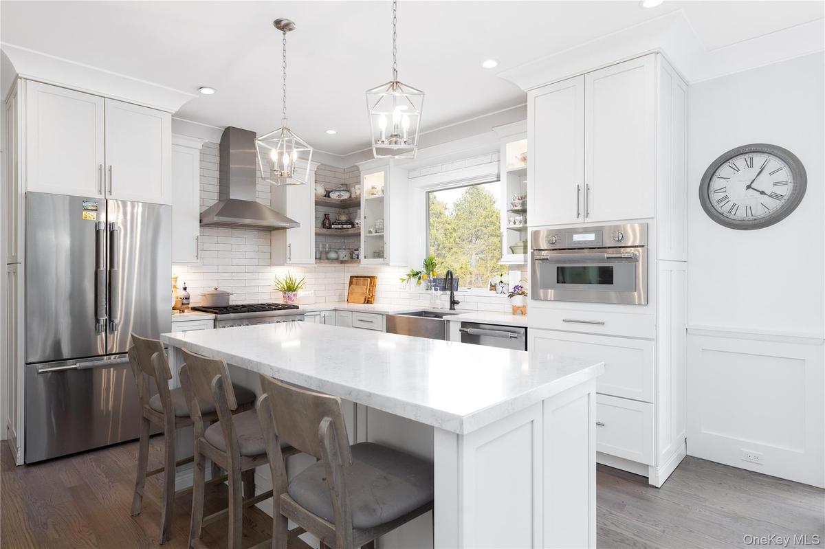 Kitchen with stainless steel appliances, a breakfast bar, pendant lighting, wall chimney range hood, and light stone countertops