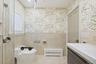Full bathroom featuring a wainscoted wall, radiator, tile walls, vanity, and wallpapered walls