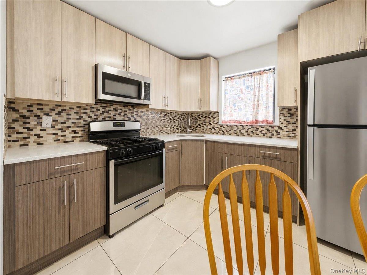 Kitchen featuring two-tone cabinetry with stainless steel hardware, a mosaic tile backsplash, white countertops, and white tile flooring