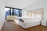 Primary Bedroom with Expansive windows showcasing cityscape views, light wood-finish flooring, white walls, and a paneled upholstered headboard