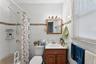 Bathroom featuring white subway tile walls with a decorative mosaic accent band, a built-in bathtub with shower, a single vanity with wood-finish cabi